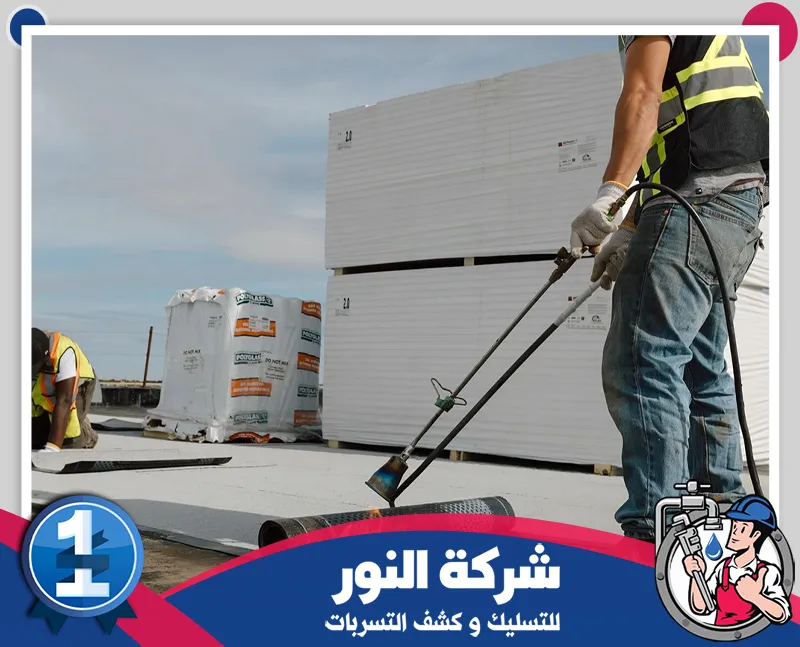 شركة عزل اسطح بالطائف | 0546824999 | شركة النور رجل يستخدم أداة المشعل لفرد وتركيب رول العزل، مما يدل على براعته الحرفية في بيئة البناء.