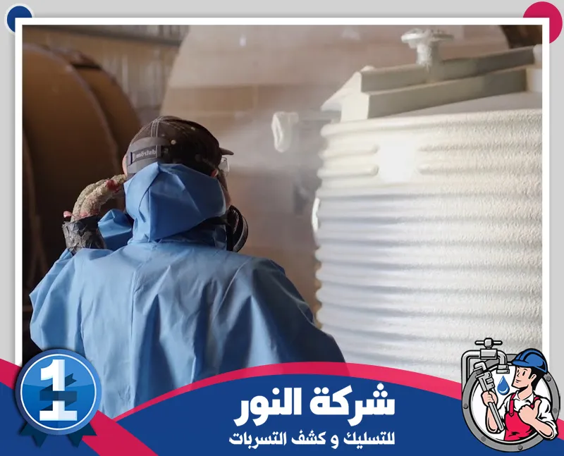 شركة عزل اسطح بالطائف | 0546824999 | شركة النور رجل يرتدي سترة زرقاء يرش مادة العزل على خزان أبيض، موضحاً تقنيات عزل الأسطح في الطائف.
