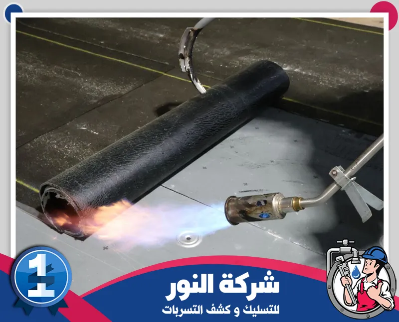 انواع عزل الاسطح | شركة النور للتسليك عامل يستخدم جهاز تسخين لتثبيت لفائف العزل على سطح المبنى لضمان إحكام الطبقات، ضمن أعمال شركة عزل اسطح بالنعيرية لمنع تسرب المياه وحماية الأسطح.