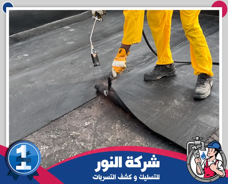عزل حراري للاسطح | شركة النور للتسليك فني يرتدي ملابس العمل ويطبق مادة عزل على سطح المبنى باستخدام أدوات مخصصة لتغطية السطح بالكامل، ضمن خدمات شركة عزل اسطح بالنعيرية لحماية المباني من الرطوبة والتسربات.